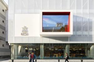 Three people walk by a contemporary building with RCSI logo on it.